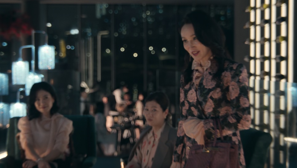 A Jeong Yeo-jin de pé num bar à meia-luz, de blusa florida, sorrindo para as pessoas sentadas à mesa