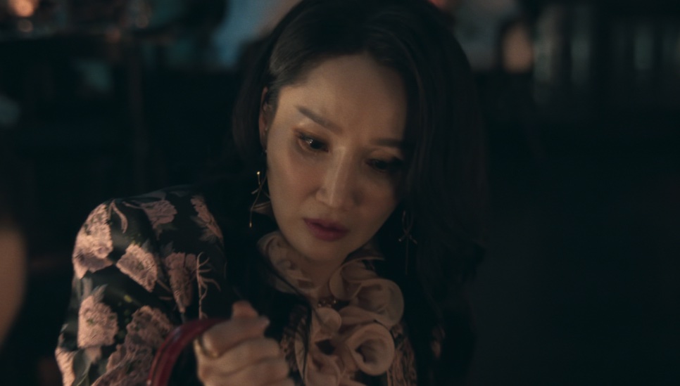 A Jeong Yeo-jin olhando para baixo, surpresa, segurando a alça de uma bolsa vermelha