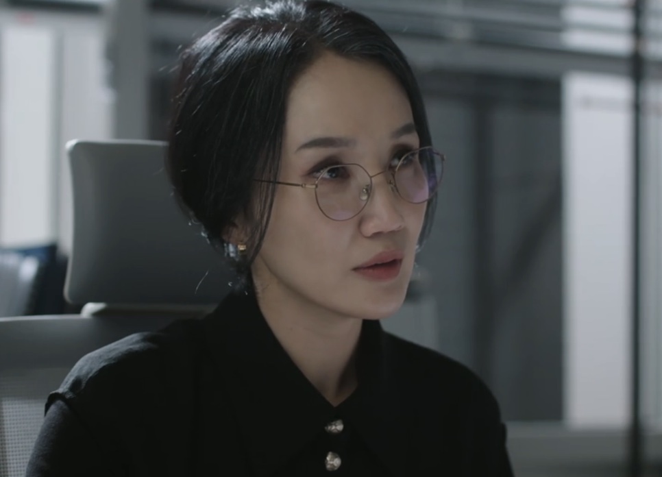 Park Bo-kyung de óculos e camisa preta, com o cabelo preso, num escritório, no papel de Park Hyeon-suk em The Ordinary Jackpot