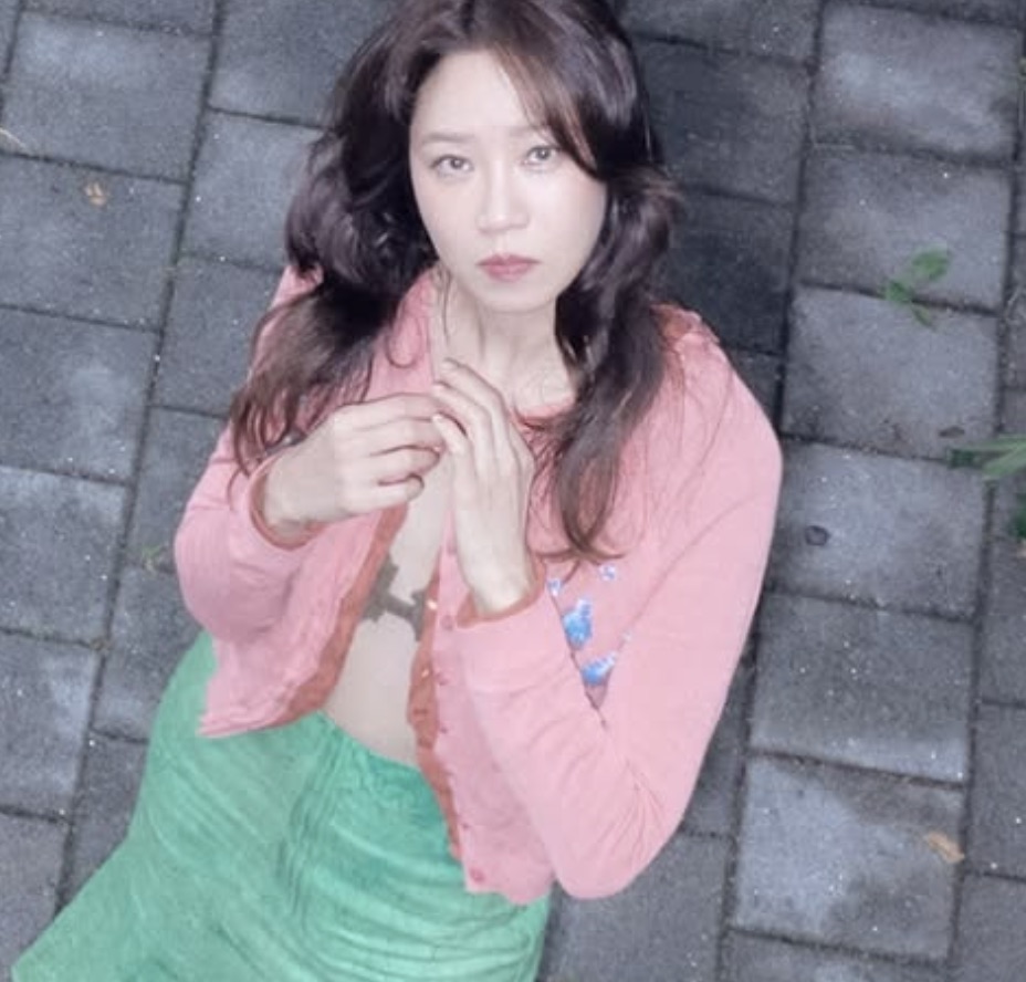 Gong Hyo-jin de cardigã rosa, deitada sobre um calçamento de pedra