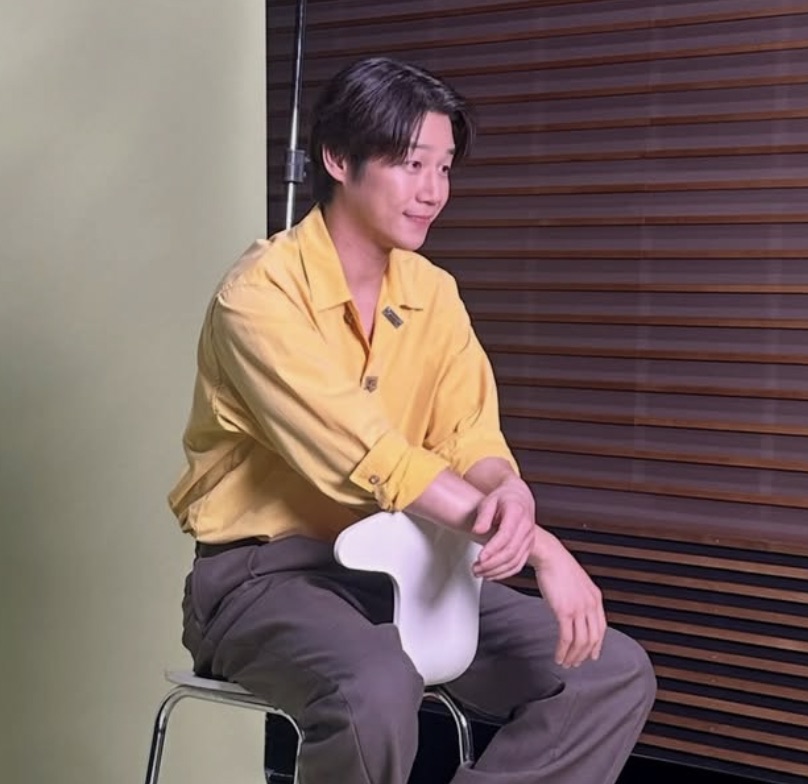 Jung Joon-won de camisa amarela, sentado numa cadeira branca