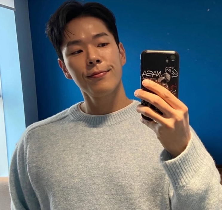 Joo Yeon-woo de suéter cinza, tirando selfie no espelho com o celular