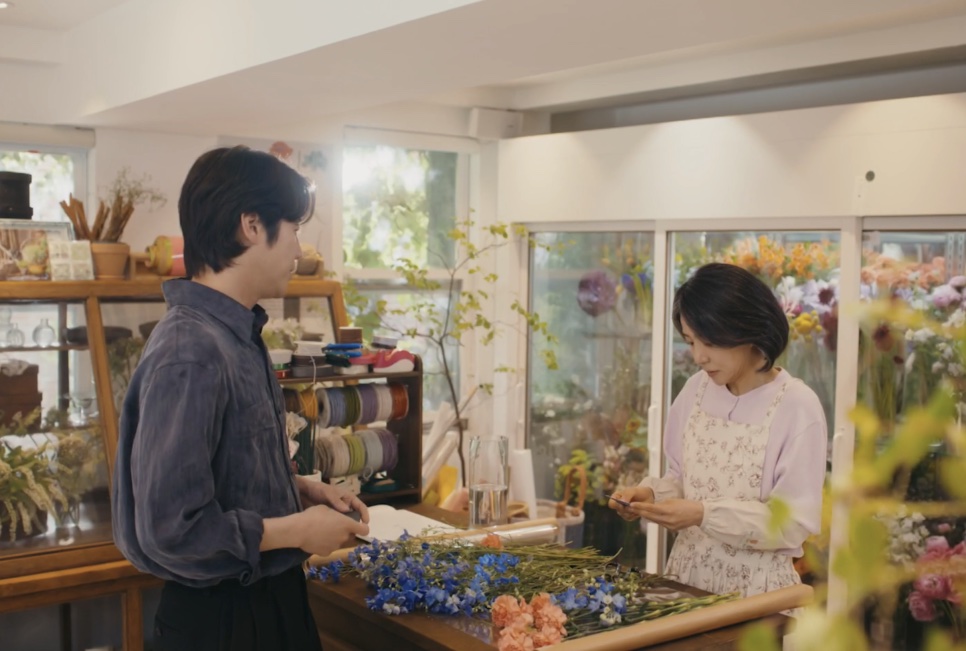 A Bae Yoon-ok montando um arranjo de flores enquanto um cliente espera no balcão