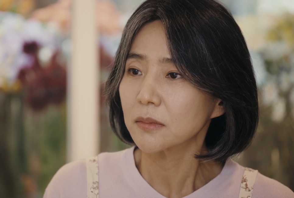 A Bae Yoon-ok de avental, com flores desfocadas ao fundo