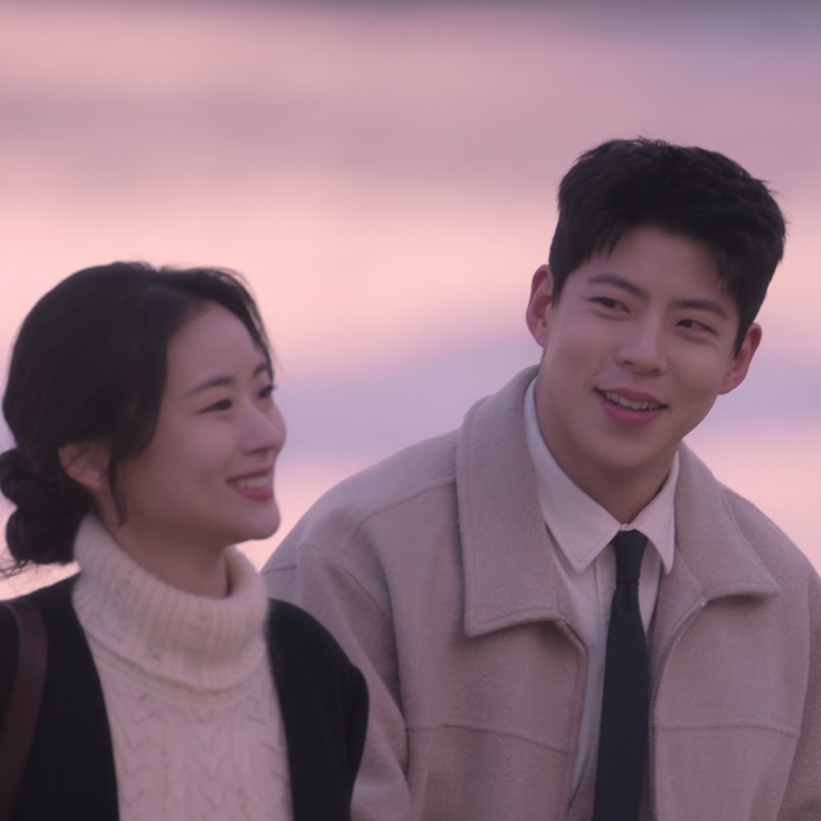 Kim Yong-woo e Shin Ji-seon sorrindo, com o céu rosado atrás