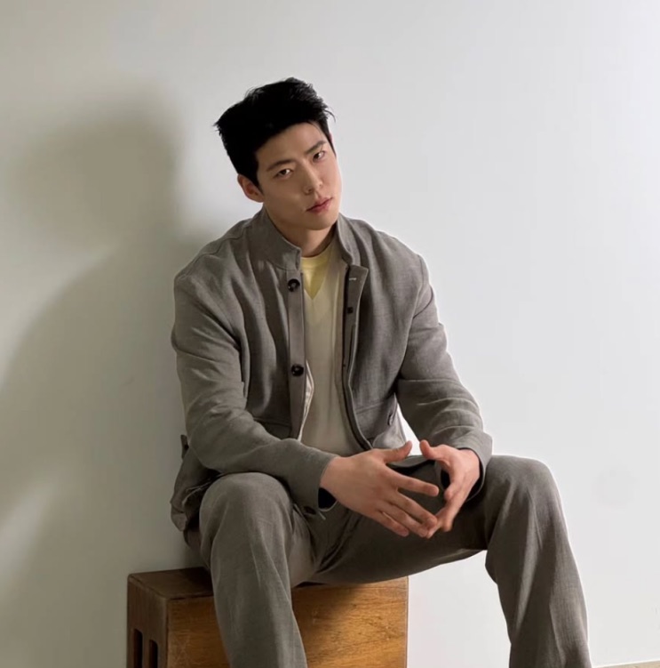 Choi Woo-sung sentado, apoiado na parede
