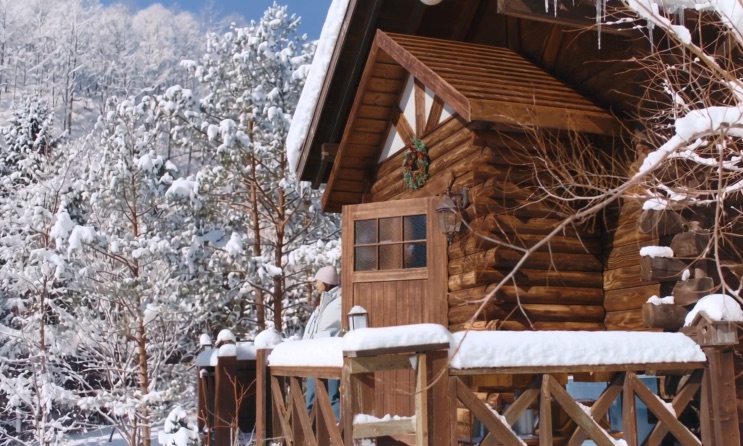 A cabana entre árvores carregadas de neve, com a varanda lateral à mostra