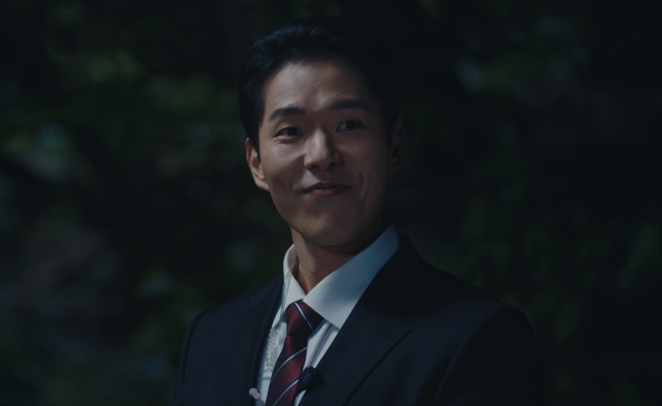 Bae Bi-ji de terno, sorrindo de leve à noite, em cena de A Bona Fide Killer