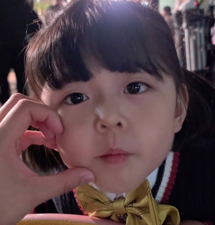 Rosto da menina em close, com laço no cabelo, fazendo pose