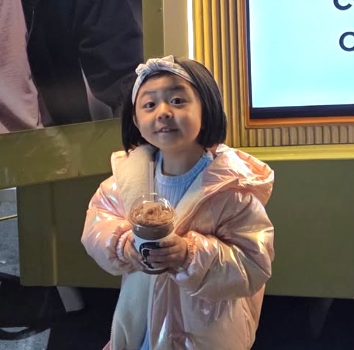 A menina de casaco azul segurando uma bebida