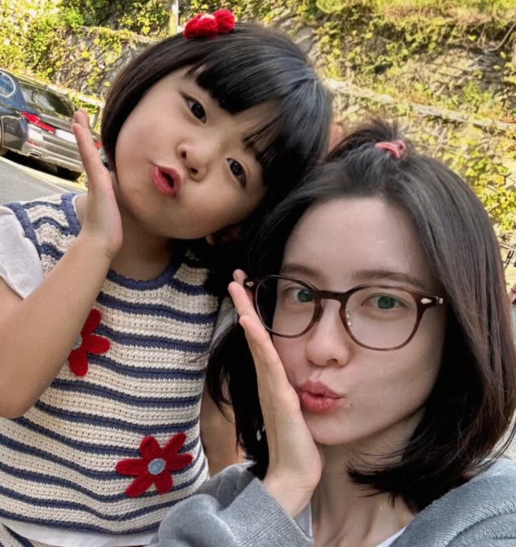 A menina fazendo pose ao lado de uma mulher de óculos, numa selfie