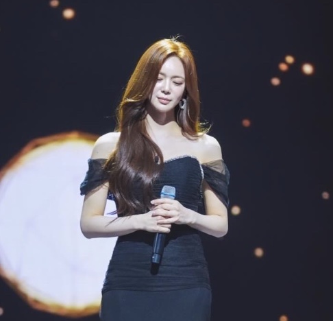Lee Elijah de vestido preto, segurando um microfone num palco