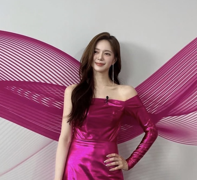 Lee Elijah de vestido rosa metálico, posando diante de um painel rosa