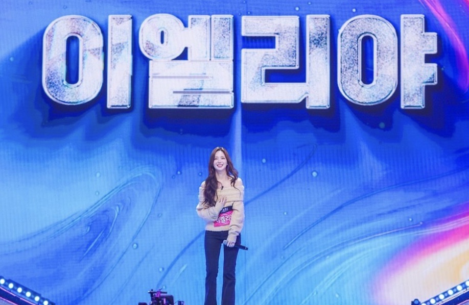 Lee Elijah cantando num palco azul, com o nome dela em letras gigantes no telão ao fundo