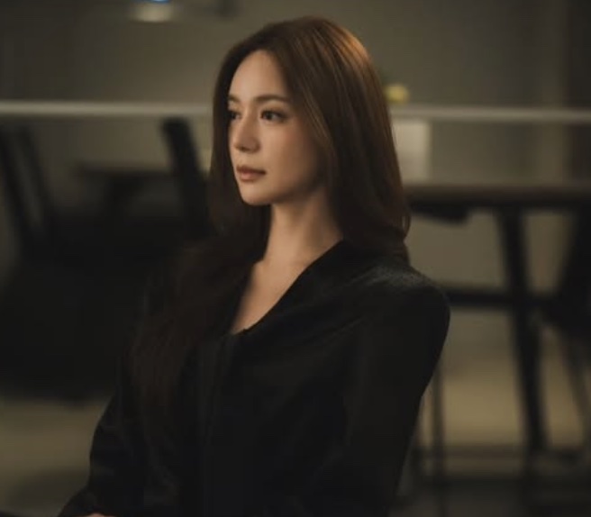 Lee Elijah de cabelo solto e roupa preta, sentada num ambiente escuro, em cena de Siren