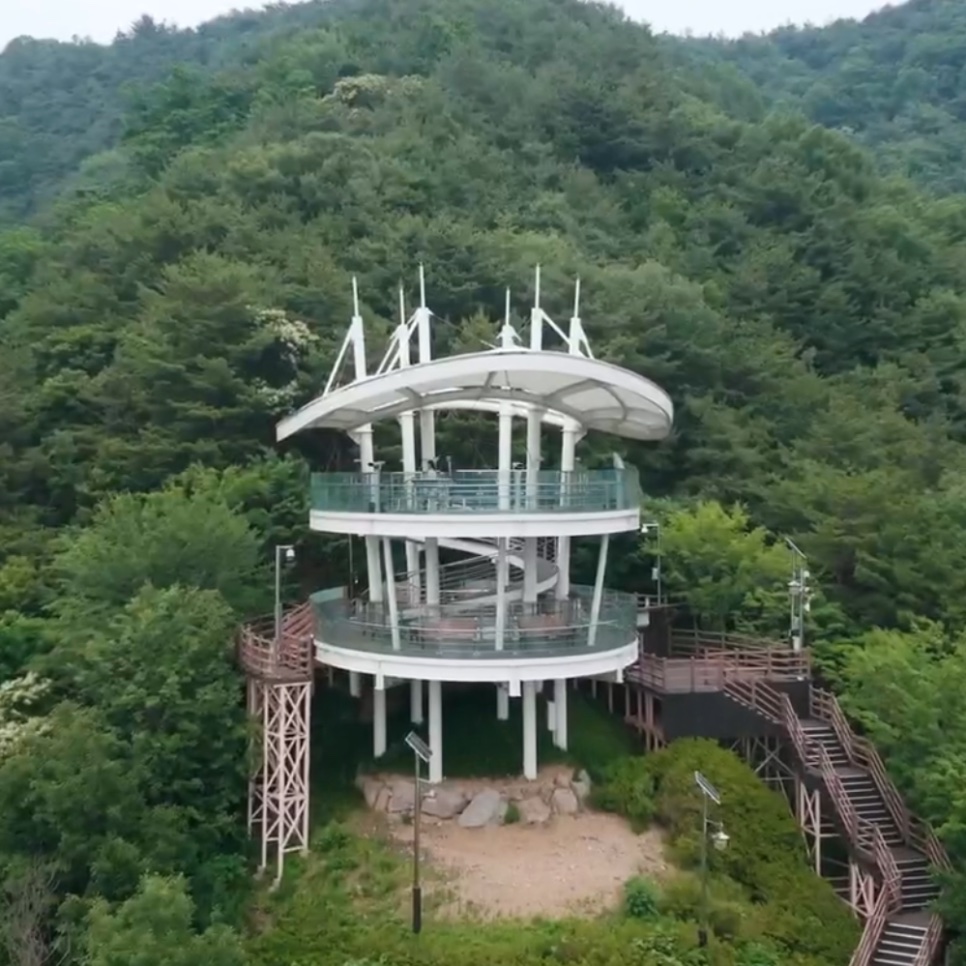 Mirante branco de dois andares no alto de um morro coberto de mata verde, visto de cima