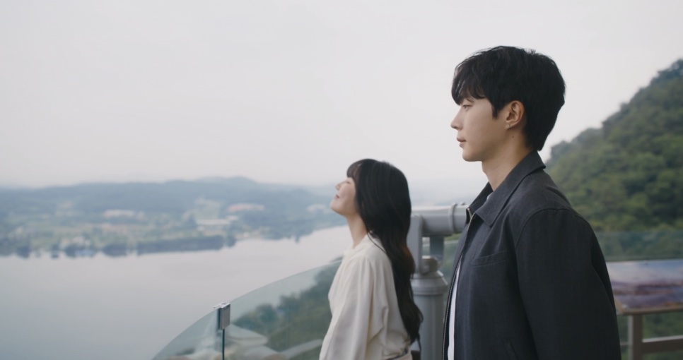 Kwon Se-a e Gi Yeong-do lado a lado no mirante, com o rio ao fundo