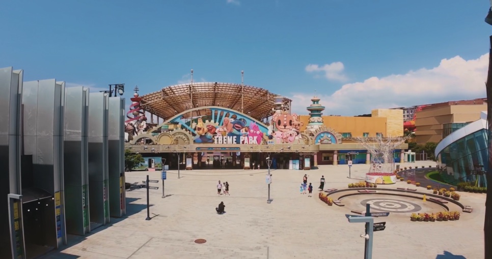 Praça de entrada do parque de diversões, com um portal colorido e céu azul