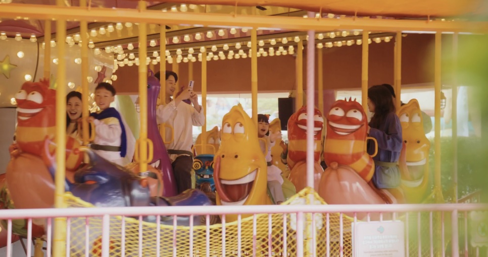 A família de Bo-na num carrossel decorado com os personagens do desenho Larva
