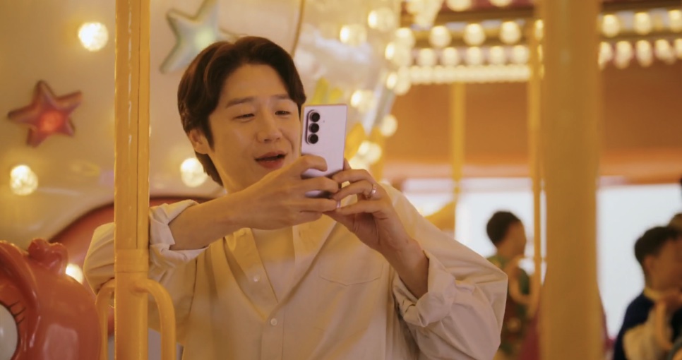 Kwon Tae-seong filmando com o celular, sentado no carrossel