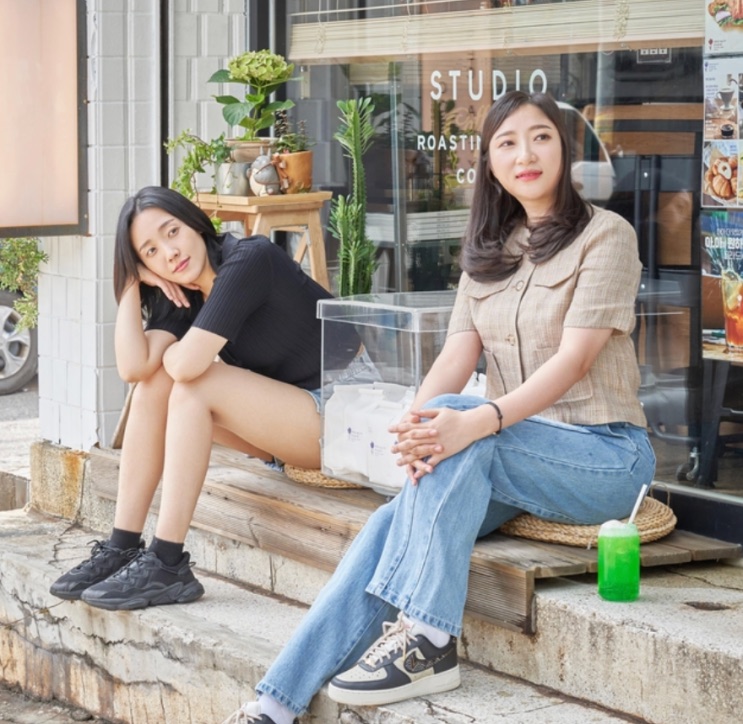 Duas mulheres sentadas na escada de um estúdio, em foto posada