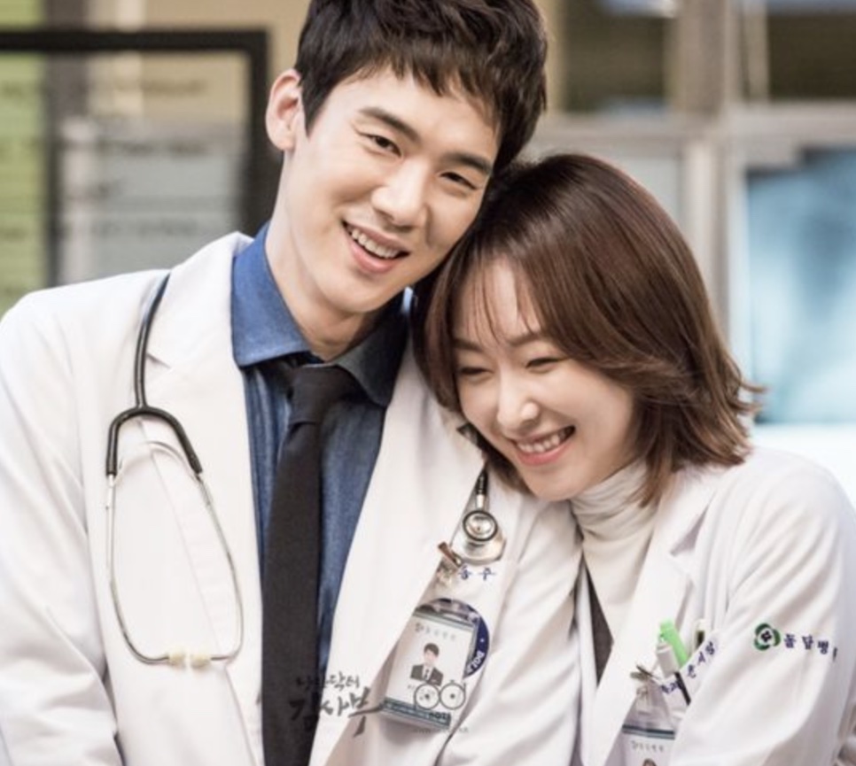 Yoo Yeon-seok e Seo Hyun-jin de jaleco, sorrindo abraçados, como Gang Dong-ju e Yun Seo-jeong em Dr. Romântico