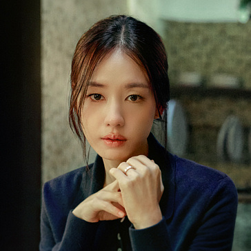 Ahn Eun-jin de cardigã azul, com as mãos entrelaçadas perto do rosto, em uma cena de dorama