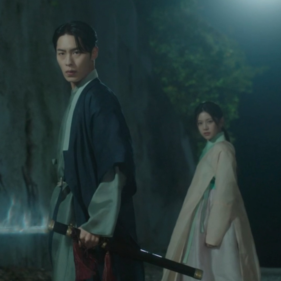 Lee Jae-wook, no papel de Jang Uk, segurando uma espada à noite, com Go Youn-jung, no papel de Jo-yeong, logo atrás, em Alquimia das Almas