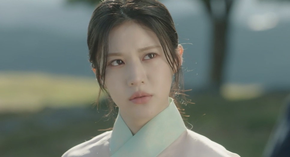 Close de Go Youn-jung, no papel de Jo-yeong, de hanbok claro, olhando para o lado ao ar livre