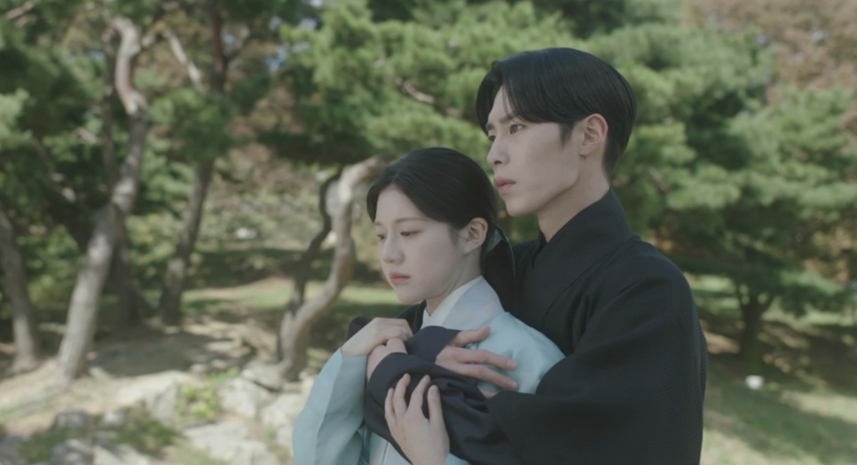 Jang Uk abraçando Jo-yeong por trás, no meio de pinheiros