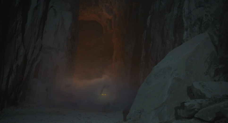 Entrada escura de uma caverna entre rochas, com uma luz fraca lá dentro