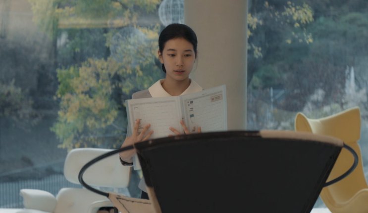 Suzy atrás de um púlpito, lendo um caderno diante de uma plateia