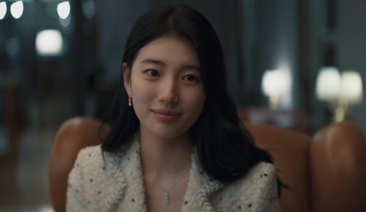 Suzy de jaqueta de tweed clara, sorrindo em um salão com luz quente