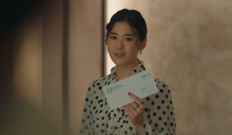 Suzy de vestido de poá, segurando um envelope diante do corpo