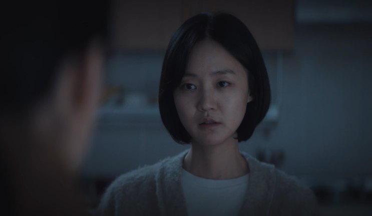 Park Ye-young de cabelo curto e cardigã claro, em um ambiente escuro