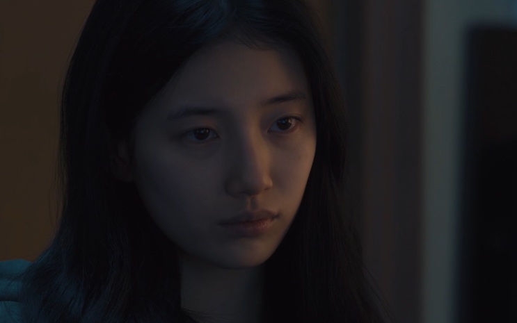 Lee Yu-mi de cabelo solto, com expressão fechada, em um ambiente escuro