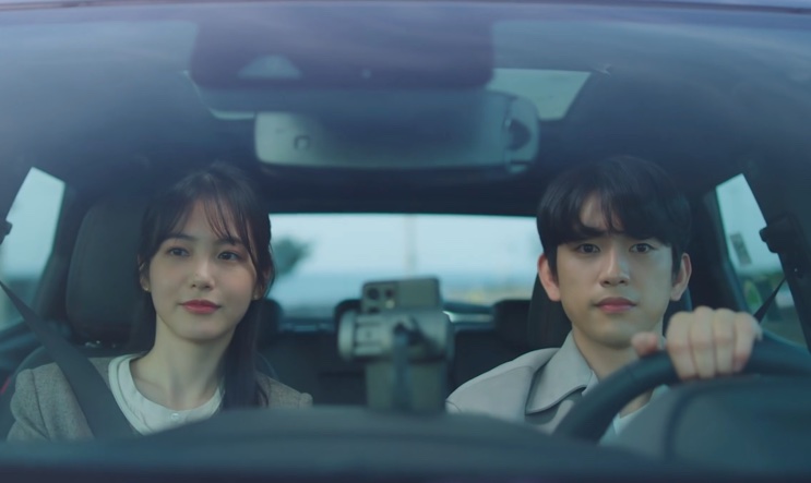 Yumi e Yoo Babi sorrindo dentro do carro, ele ao volante