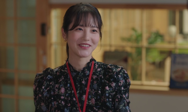 Uma colega de trabalho sorrindo no escritório, de vestido florido e crachá
