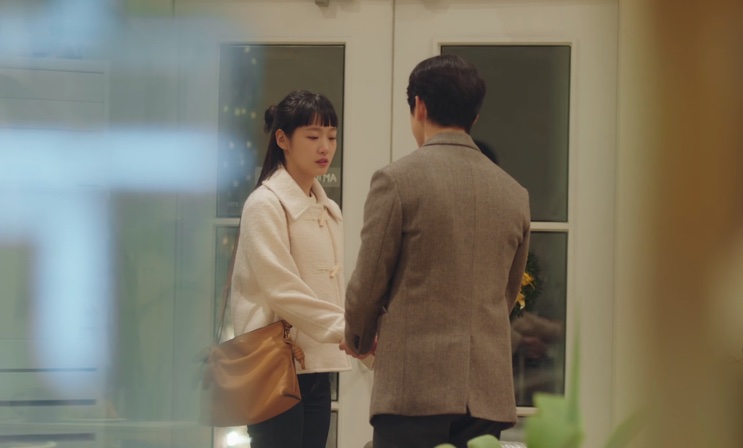 Um casal conversando na porta de um prédio, visto através do vidro