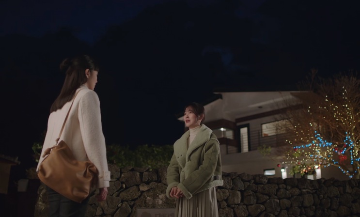 Duas mulheres conversando à noite, em frente a um muro de pedra