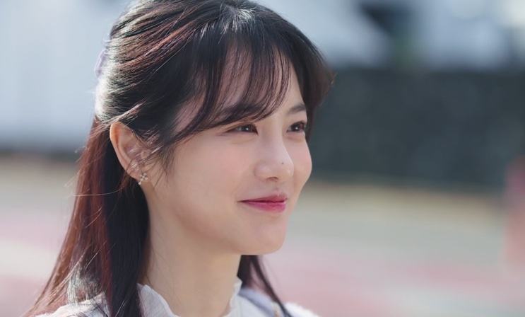 Mulher de perfil, sorrindo, em uma área externa clara