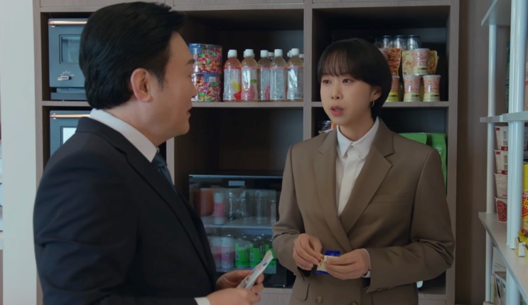 Bong Ji-uk de terno conversando com um homem mais novo, numa despensa