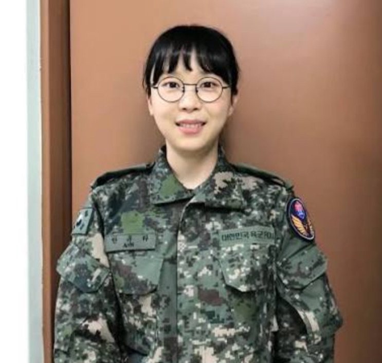 Kim Han-na de uniforme militar camuflado e óculos, sorrindo