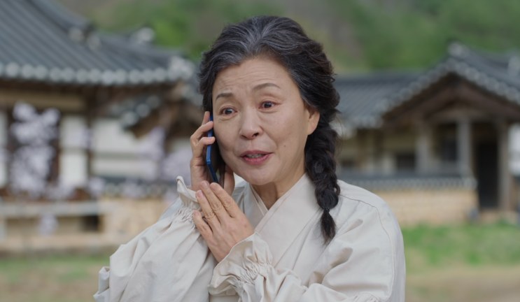 A Paeng Myo-sun ao telefone, em frente a uma construção tradicional