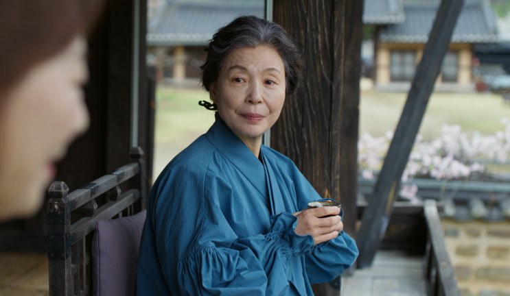 A Paeng Myo-sun de hanbok azul conversando com alguém numa casa tradicional