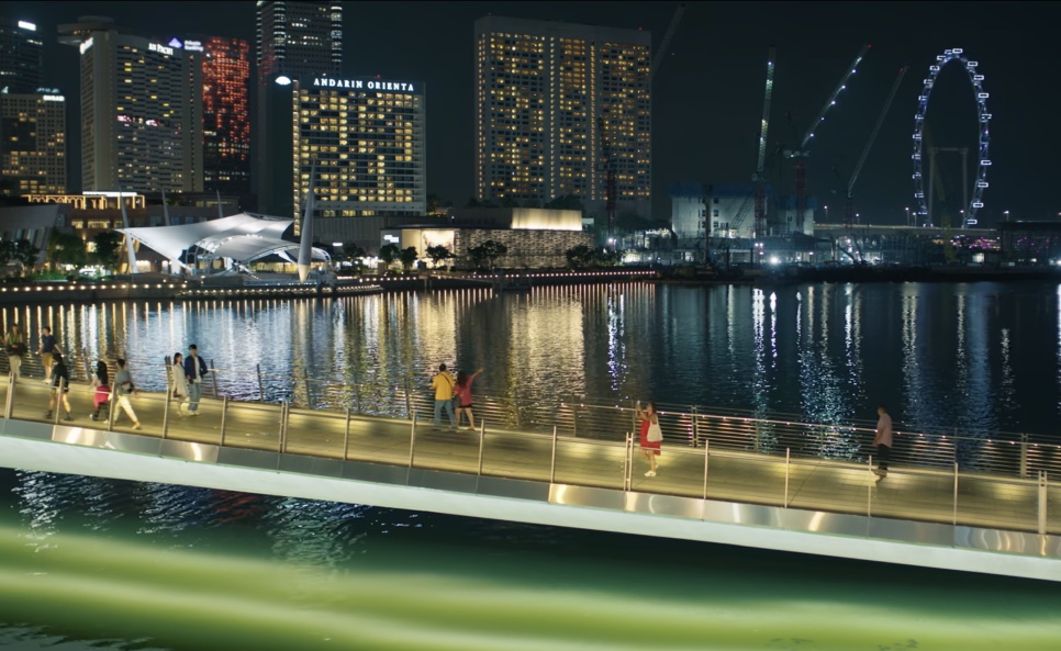 A orla da baía à noite, com os prédios iluminados e a roda-gigante ao fundo