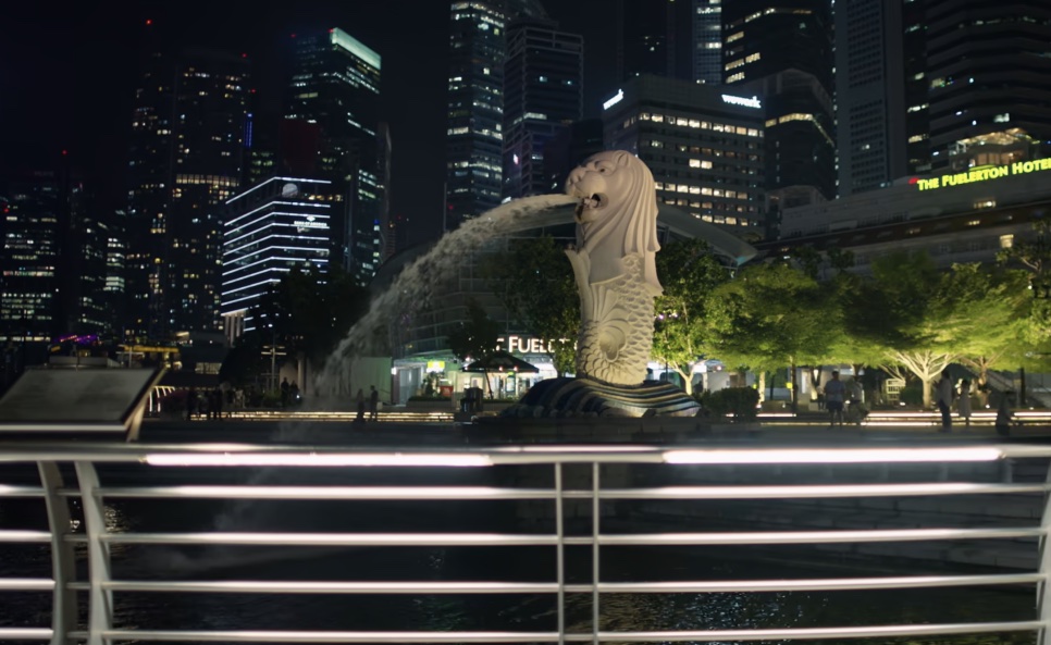 O Merlion jorrando água à noite, com os prédios do centro atrás