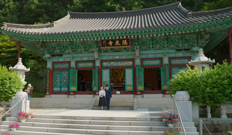 Fachada do salão principal do templo, com portas de treliça verdes e um casal parado na escadaria
