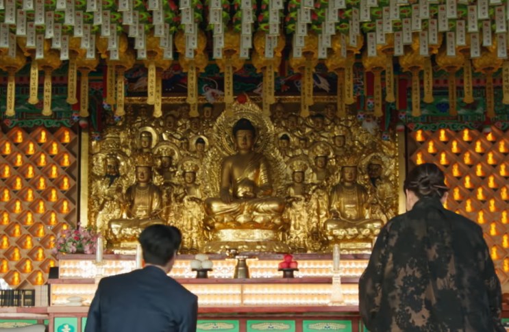 Estátua dourada de Buda no altar do salão, vista por trás de duas pessoas ajoelhadas