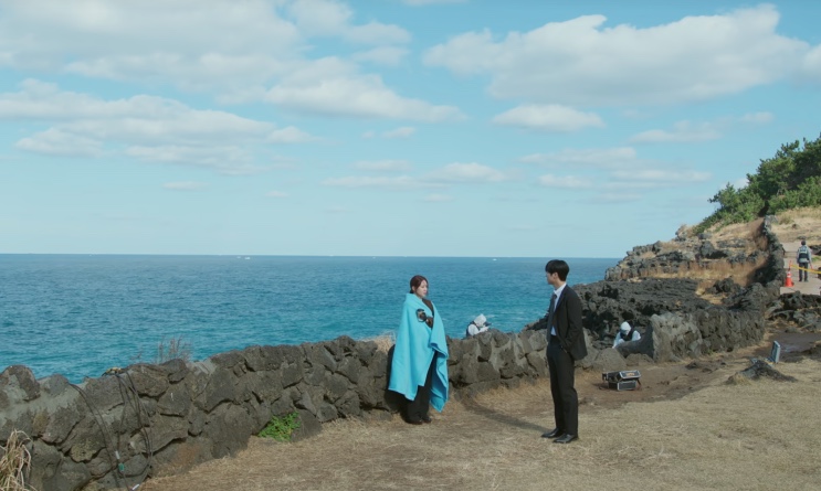 Yeo-ri enrolada no cobertor e Kang-wook conversando à beira do mar
